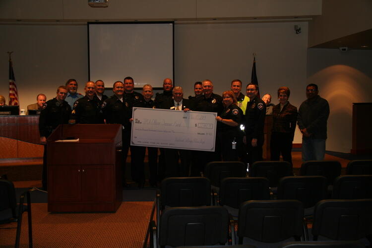 A group of officers standing together holding a large check donated by Highland Village police department.