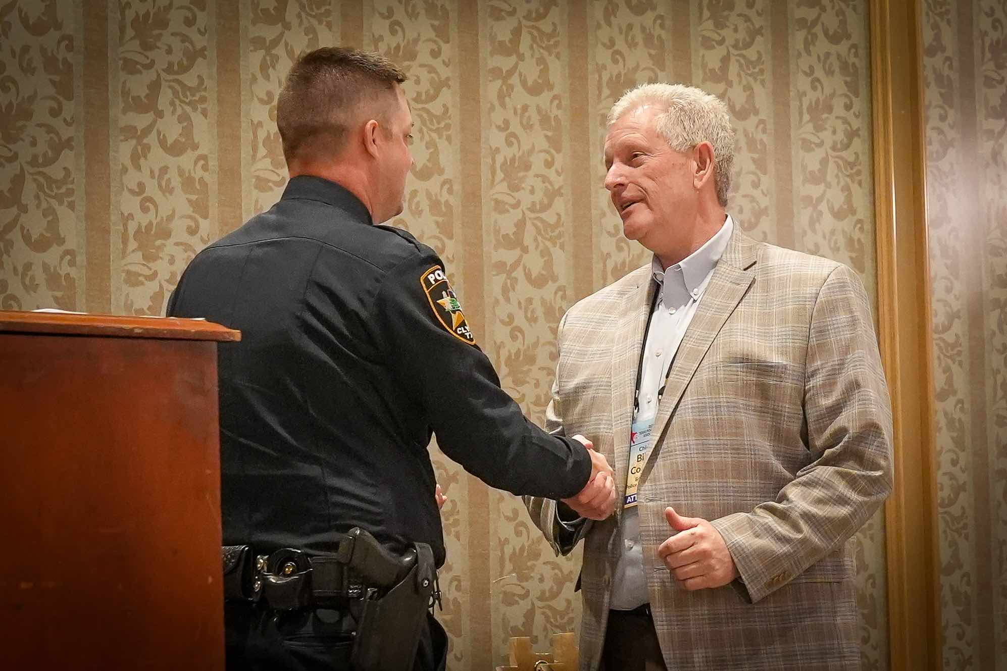 Two white male police officers shake hands.